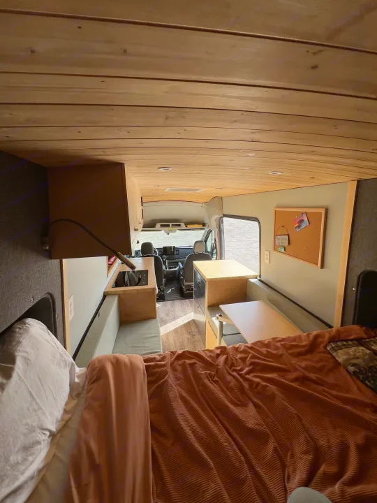 Explore this custom RV rental, featuring a comfortable bed, functional kitchen, and dining/lounge area, perfect for travel.. Ford Transit 2022