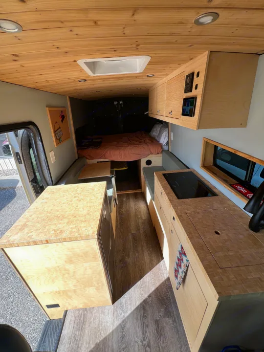 Spacious, modern camper van interior, perfect for your next RV rental adventure. Features wood accents, kitchen, and cozy bed.. Ford Transit 2022