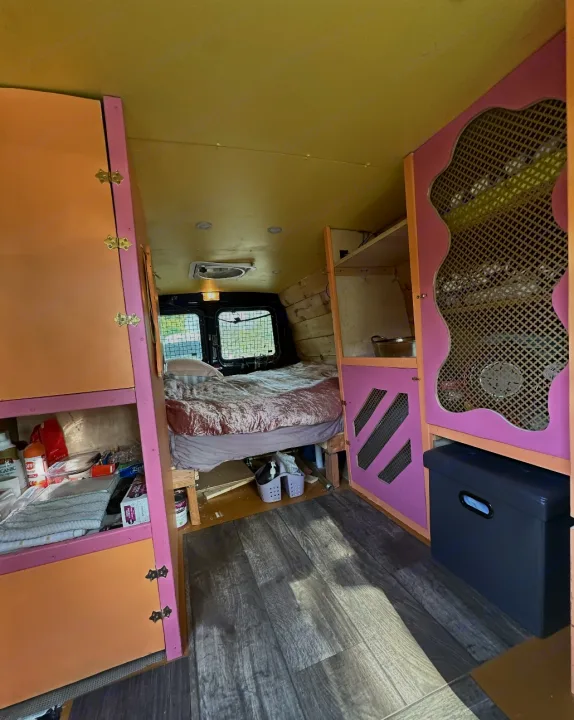 Cozy RV rental camper van interior. Features a bed, vibrant pink & orange custom cabinetry, and wood-look flooring.. Ford Econoline 2010