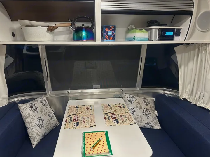 RV rental interior showing a cozy dining area with placemats, kitchen shelf with kettle, and entertainment system.. Airstream Bambi 2022