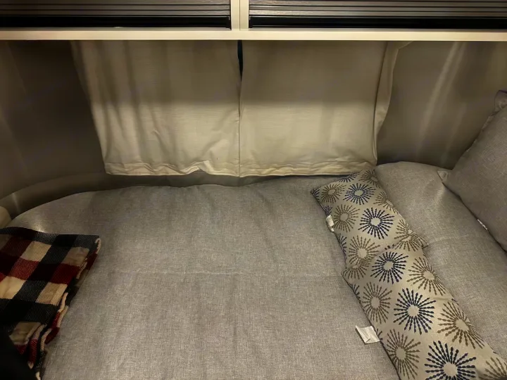 Cozy RV rental bed features light gray linens, a red plaid blanket, and patterned pillows. Perfect for a comfortable travel trailer trip.. Airstream Bambi 2022