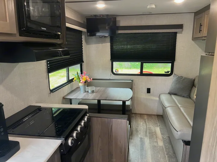 Inside a modern RV rental: a bright living space with kitchen, dining booth, sofa, and TV for comfortable travel.. Gulf Stream Ameri-Lite 2022