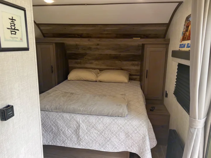 Cozy RV rental bedroom features a comfortable queen bed with rustic wood headboard and built-in storage.. Gulf Stream Ameri-Lite 2022
