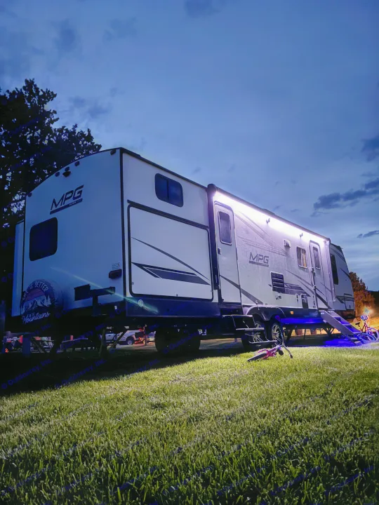 Night view of a modern RV rental with bright awning lights and cool blue underglow, parked on grass. A great camping setup!. Other Other 2021