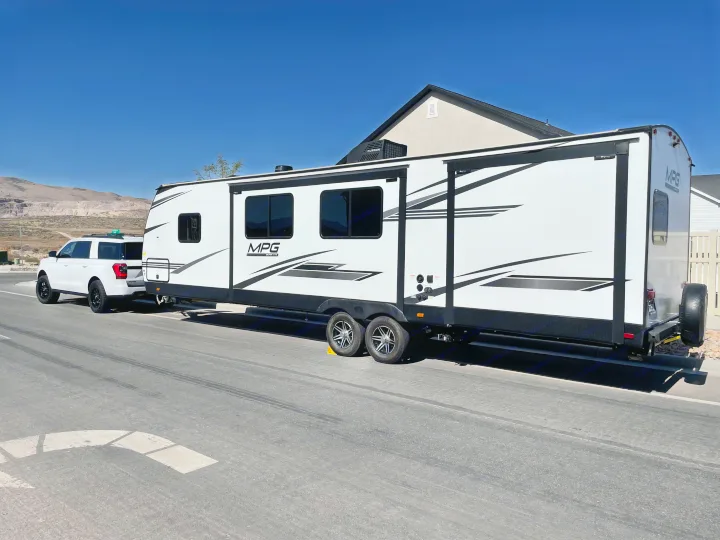 White Ford Expedition SUV towing a large white travel trailer (RV) on a paved road with mountains. Ideal for an rv rental.. Other Other 2021