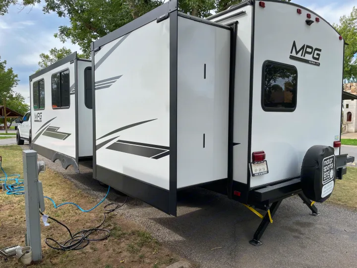 White MPG Ultra-Lite travel trailer, likely an RV rental from Motor Sportsland, with its slide-outs extended at a campsite.. Other Other 2021