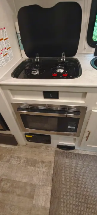 Compact RV rental kitchen with stove, microwave, and sink. Perfect for preparing meals on the go.. Forest River R-Pod 2023