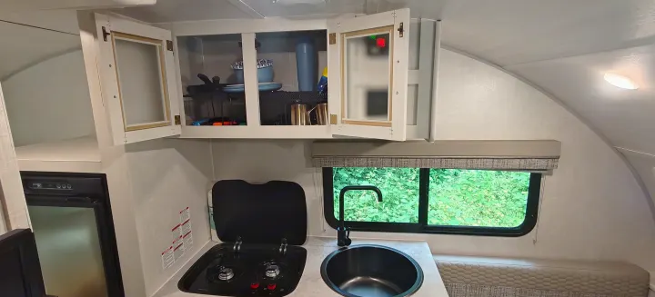 An RV rental's kitchen, showcasing compact efficiency: stove, sink, fridge, and open overhead storage.. Forest River R-Pod 2023
