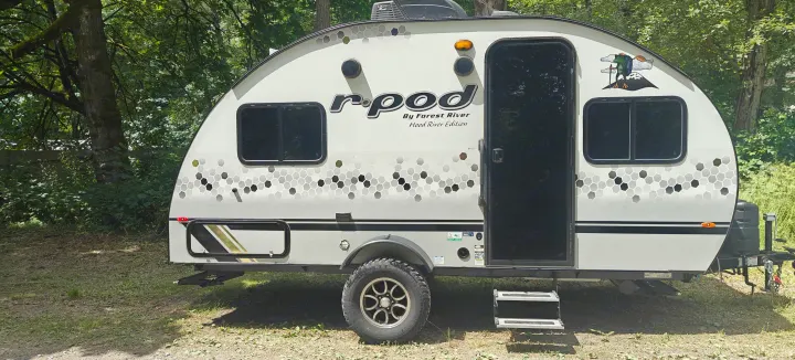 This r-pod RV rental is a compact travel trailer, featuring hexagonal graphics, parked in a wooded area for camping.. Forest River R-Pod 2023
