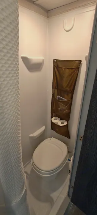 Compact RV rental bathroom features a toilet, shower area with curtain, and wall-mounted storage.. Forest River R-Pod 2023
