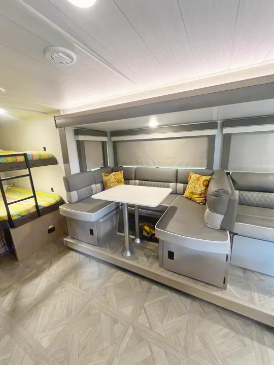 Spacious RV rental interior with a gray dinette, white table, and vibrant bunk beds for comfortable travel.. Forest River Wildwood X-Lite Platinum 2024