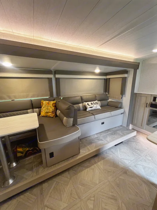 Step inside this RV rental's modern living area! It features an L-shaped sofa, adjustable table, and stylish lighting.. Forest River Wildwood X-Lite Platinum 2024