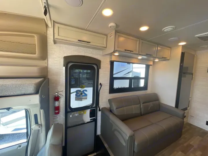Inside an **rv rental**: view of the functional interior with a sofa, bunk, overhead cabinets, fridge, and entry door.. Jayco Greyhawk 2026