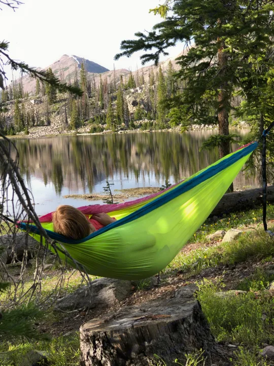 Person relaxing in a colorful hammock by a tranquil lake and mountains, a serene spot on your RV rental journey.. Kia EV6 Wind All Wheel Drive 2022