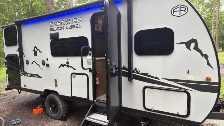 Bright white Cherokee Black Label RV rental with mountain graphics & blue lights, parked at a campsite.. Forest River Cherokee Wolf Pup 2025