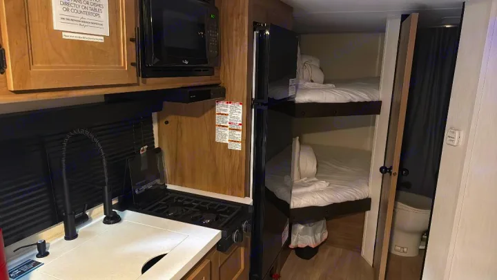 This RV rental offers a kitchen with stove, sink, bunk beds, and a compact bathroom visible beyond.. Forest River Cherokee Wolf Pup 2025