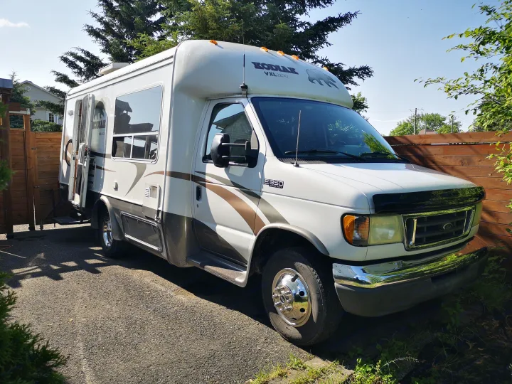 A white and brown Kodiak Class C RV, perfect for your next rv rental adventure, parked on a gravel driveway.. Ford F350 2003