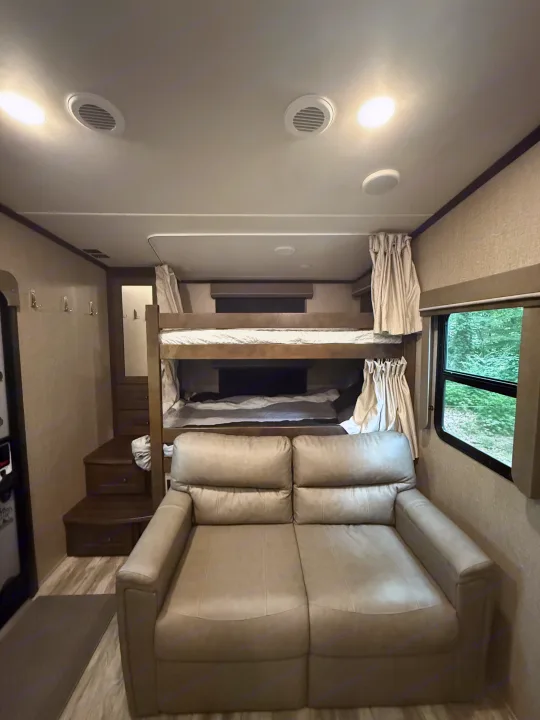 RV rental interior: cozy living area with light sofa, bunk beds, storage steps, and a scenic window.. Grand Design Reflection 2020