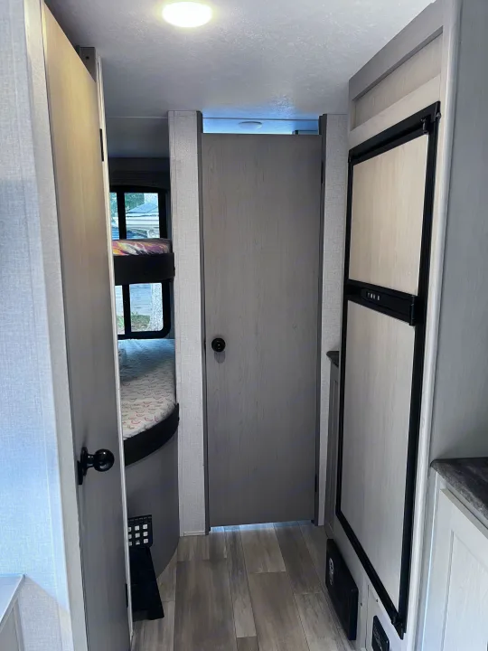 This RV rental's interior shows a hallway. Bunk beds are on the left, a door center, and a refrigerator right.. Clipper 4K 2023