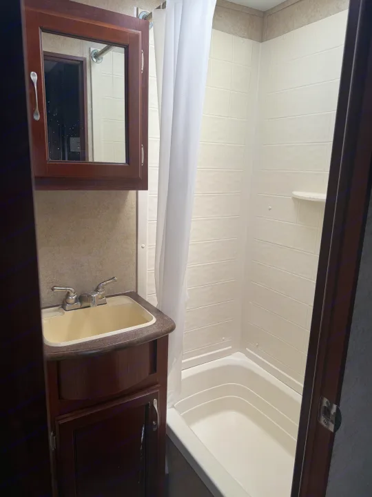 Inside an RV rental, this compact bathroom features a vanity, sink, mirror cabinet, shower with curtain, and a small tub.. Evergreen RV Ascend 2015