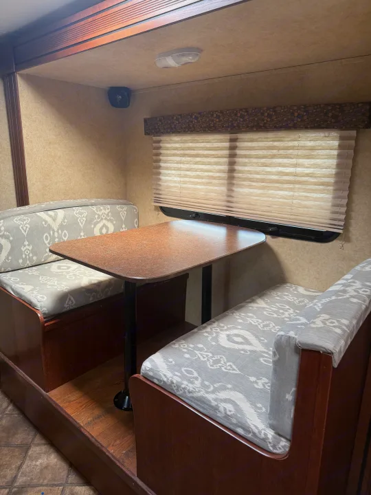 Cozy RV rental dinette featuring a table and two upholstered benches with grey patterned cushions. Ideal for travel.. Evergreen RV Ascend 2015