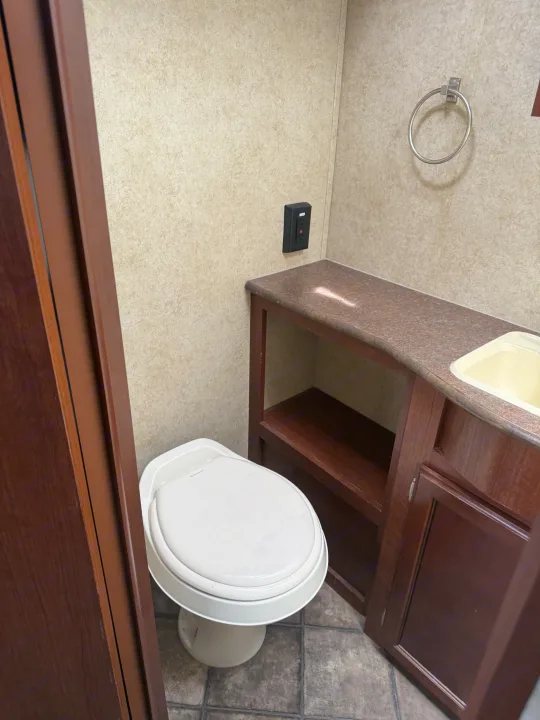 Clean RV rental bathroom interior, featuring a white Dometic toilet, wood vanity with sink, and towel ring.. Evergreen RV Ascend 2015