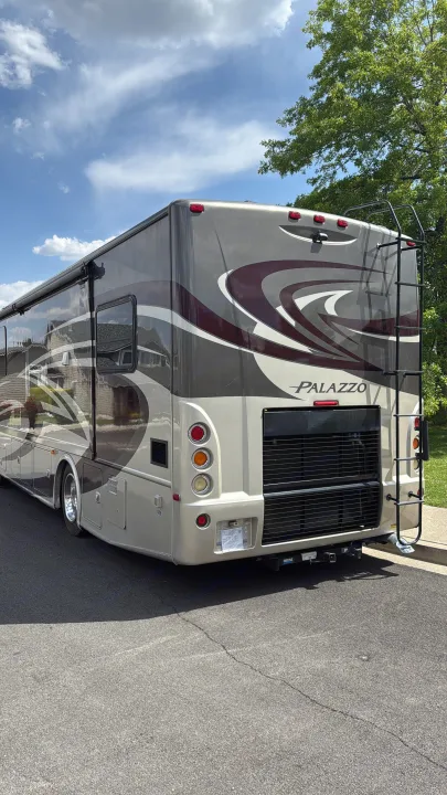 Rear view of a large, two-tone Palazzo motorhome, perfect for rv rental. Features a rear ladder and tow hitch.. Thor Palazzo 2014