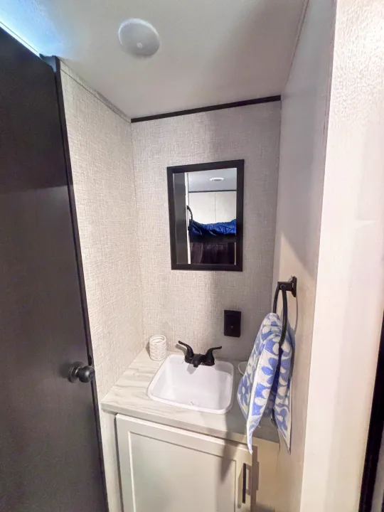Compact RV rental bathroom: white sink, black faucet, mirror reflecting a bunk, and a blue towel.. Jayco Jay Flight slx 260 bhw 2025