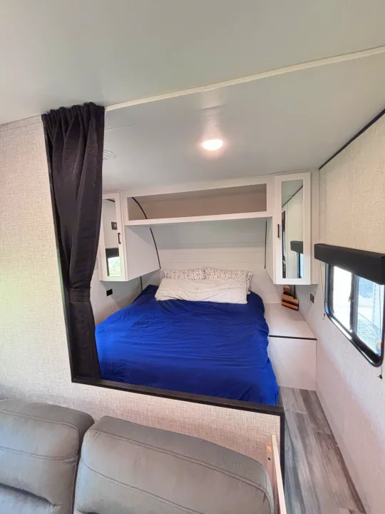 Inside an RV rental: a modern bedroom featuring a bed with blue bedding, white cabinets, and a privacy curtain.. Jayco Jay Flight slx 260 bhw 2025