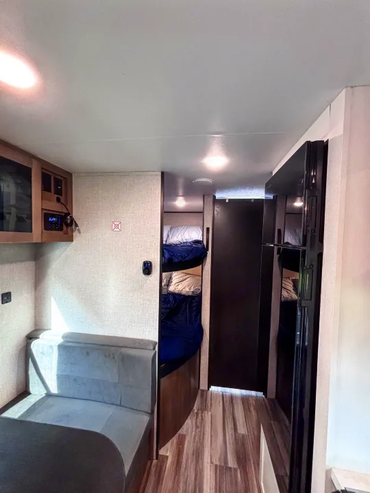 RV rental interior: A compact living space featuring a dinette, entertainment/control panel, cozy bunk beds, and a dark refrigerator.. Jayco Jay Flight slx 260 bhw 2025