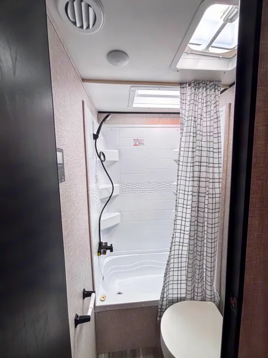 Compact rv rental bathroom featuring a white tub/shower, checkered curtain, toilet, and skylight. Clean, functional design.. Jayco Jay Flight slx 260 bhw 2025