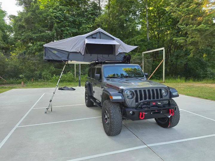 A grey Jeep Wrangler Rubicon with a deployed roof-top tent and a black cat on its roof. Perfect for an rv rental outdoor adventure.. Jeep Wrangler Unlimited Rubicon 2019