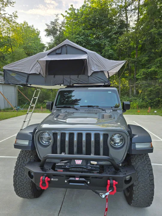 Front view of a gray Jeep with a deployed rooftop tent and ladder, an innovative RV rental for off-grid camping.. Jeep Wrangler Unlimited Rubicon 2019
