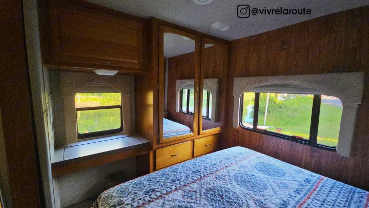 Inside your next RV rental: a bright bedroom with a quilt-covered bed, wood paneling, and mirrored wardrobe for comfortable travel.. Tioga SL 2008