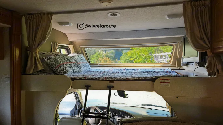 This RV rental offers a cozy cab-over bunk bed, seen with bedding, curtains, and a scenic window view.. Tioga SL 2008