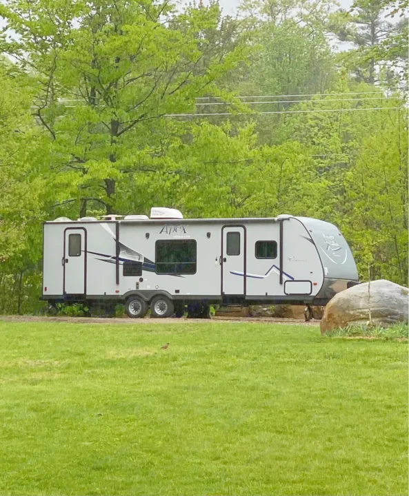 This grey Apex travel trailer rv rental is parked among lush green trees and grass, ideal for a camping getaway.. Coachmen Apex LE 2017