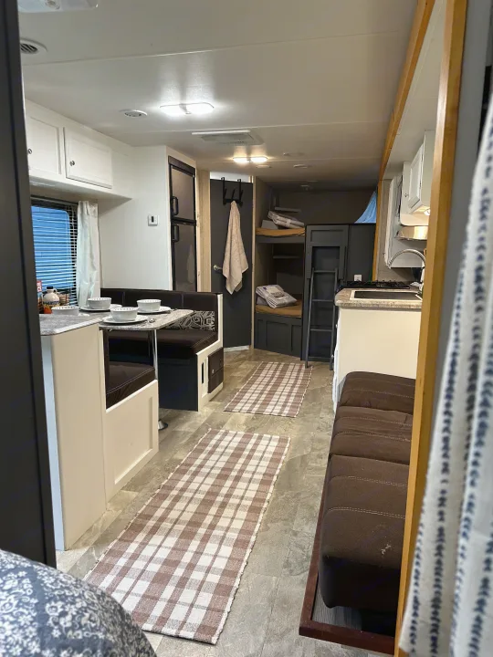 This rv rental features a well-equipped interior: a dining area, kitchen with stove, and comfortable bunk beds. Note the plaid runner rugs.. Coachmen Apex LE 2017