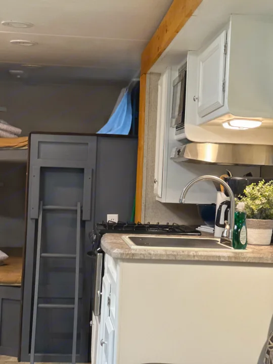 RV rental interior featuring a compact kitchen with sink and stovetop, next to bunk beds with a ladder.. Coachmen Apex LE 2017