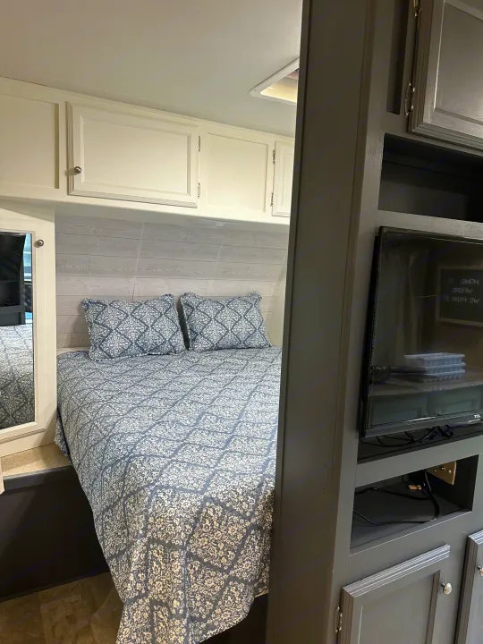 Cozy RV rental bedroom featuring patterned blue and white bedding, white cabinets, and a grey entertainment unit with a TV.. Coachmen Apex LE 2017