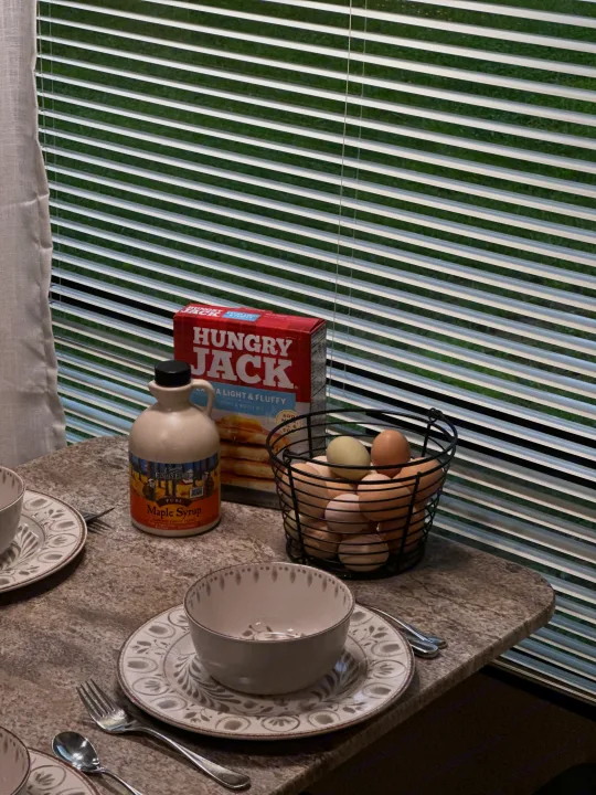Prepping breakfast in an RV rental! Eggs, maple syrup, & pancake mix are ready on the counter, with blinds showing green outside.. Coachmen Apex LE 2017
