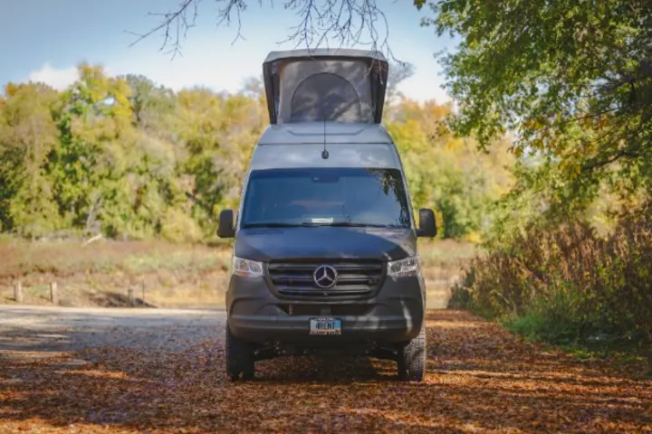 Front view of a dark Mercedes Sprinter camper van with pop-top extended, ideal for RV rental.. Mercedes Sprinter 2023