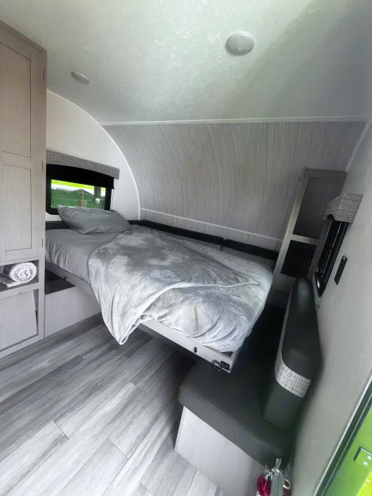Cozy rv rental interior with a comfortable bed, compact seating, and wood-look flooring, ready for your next trip.. Clipper 4K 2023