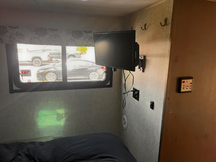 Inside an RV rental: a bedroom with an emergency exit window showing vehicles, a wall-mounted TV, and control panel.. Forester Forester Motorhome 2020
