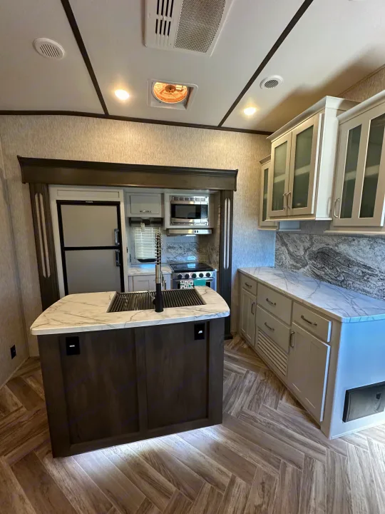 Spacious, modern RV rental kitchen featuring a central island, marble-look countertops, and stainless steel appliances.. Astoria 1500 2021