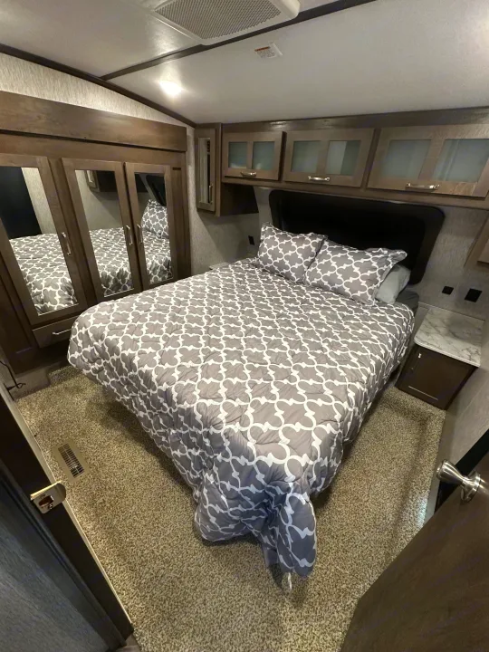 Inside a comfy RV rental bedroom: patterned bed, mirrored closet, overhead storage, and warm lighting details.. Astoria 1500 2021