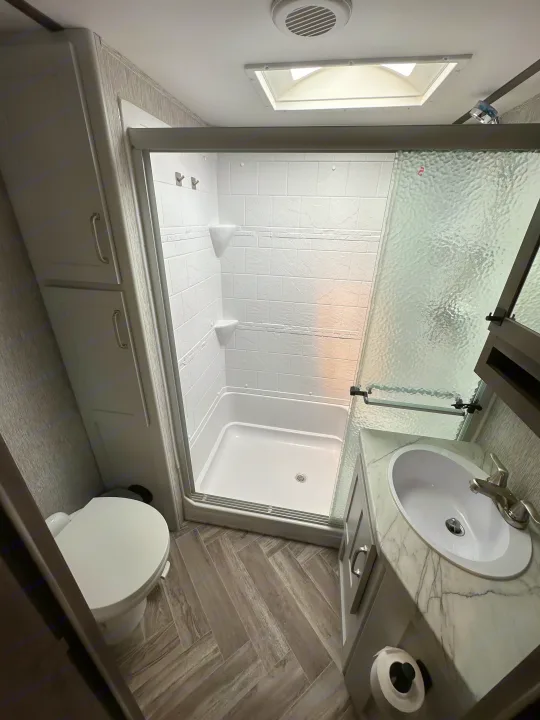 Modern RV rental bathroom featuring a shower, toilet, sink, and storage.. Astoria 1500 2021