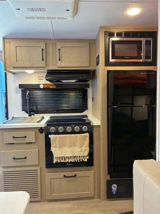 Explore the compact yet fully equipped kitchen in an rv rental, featuring Magic Chef appliances, sink, and stylish light wood cabinets.. Forest River Rockwood Geo Pro 2024