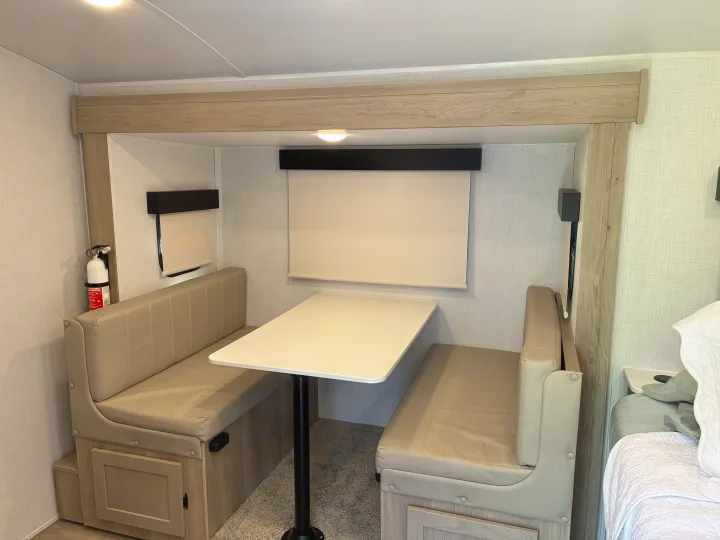 RV rental interior: a cozy dinette area with light wood & upholstered benches, a table, and visible fire extinguisher.. Forest River Rockwood Geo Pro 2024