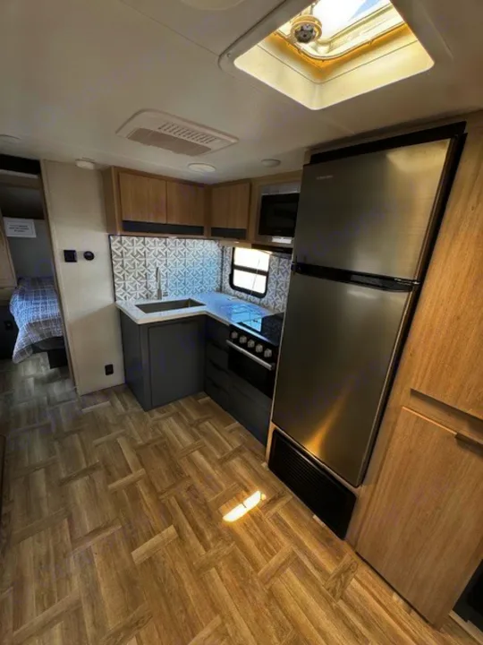 Modern RV rental interior: compact kitchen, fridge, and cozy bedroom view.. Forest River Tracer 28BHS 2024