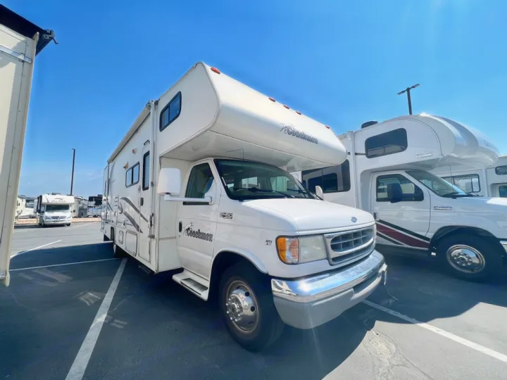 White Coachmen RV and other motorhomes in a sunny paved lot with mountains. Perfect for your next rv rental adventure.. Coachmen Leprechaun 2001
